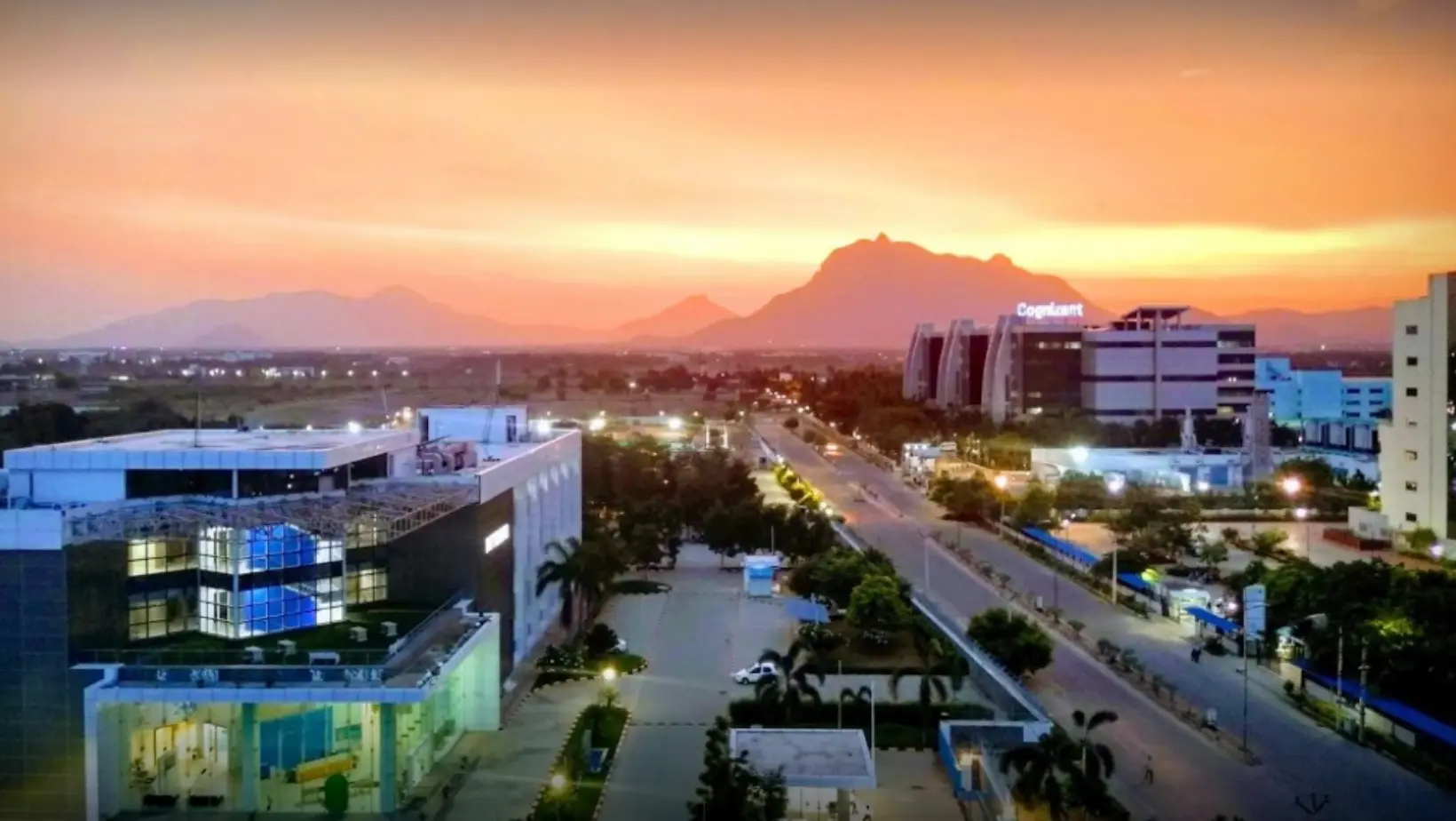 A city skyline with modern buildings is set against a backdrop of mountains under a clear blue sky.